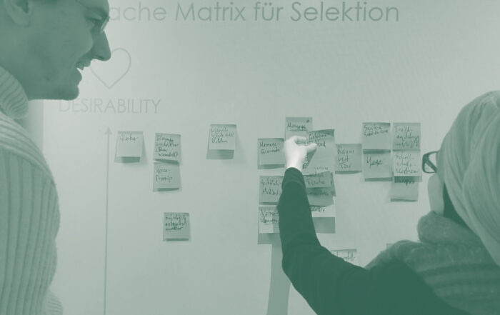 Zwei Personen sortieren Moderationskarten an einer Wand, eine Methode um schwere Entscheidungen zu treffen und Themen zu priorisieren.