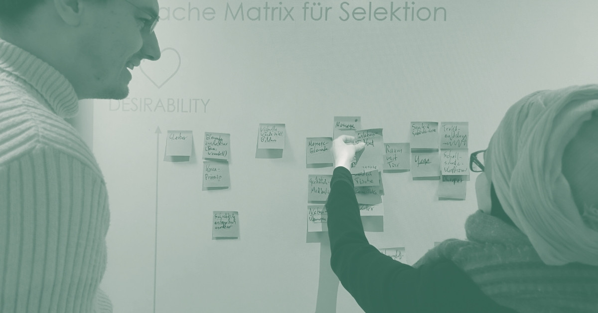 Zwei Personen sortieren Moderationskarten an einer Wand, eine Methode um schwere Entscheidungen zu treffen und Themen zu priorisieren.