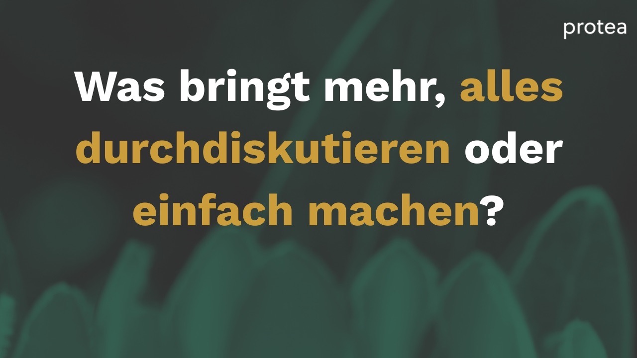 Ein Workshopraum mit vielen Flipcharts an den Wänden. Eine Teilnehmerin spricht und die anderen hören zu. 