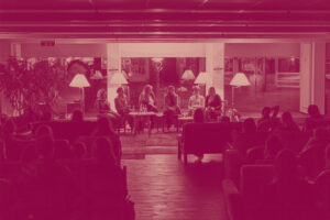Fuenf Frauen sitzen in einer Podiumsdiskussion in einem gemuetlich beleuchteten Raum. Eine der Frauen spricht in ein Mikrofon, waehrend die anderen zuhoeren. Das Publikum sitzt auf Sofas und Sesseln verteilt im Vordergrund.